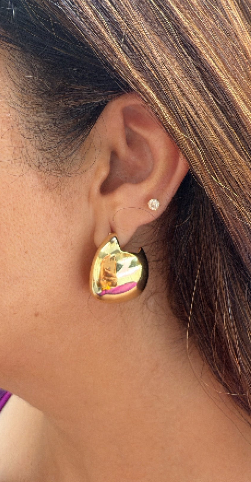 A close-up image of a woman's ear wearing a gold finish stud earring.