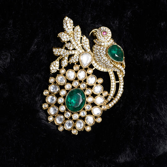 Ornate brooch with parrot design, green gemstones, and gold plaing on a black background