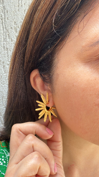Close-up of a person's ear with a gold earrings against a textured wall.