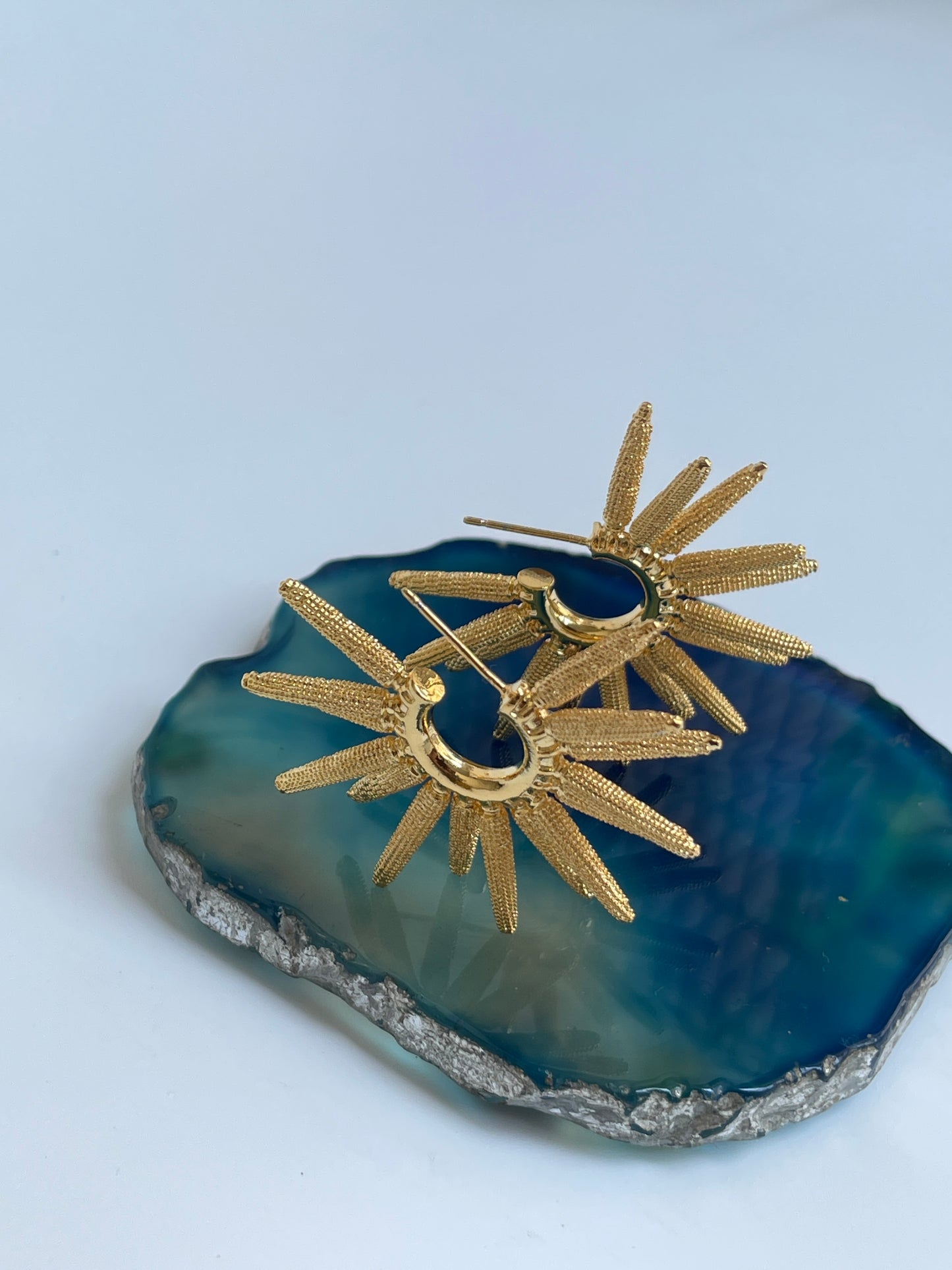 Gold plated hoop earrings by Studio6 jewels on a blue stone surface