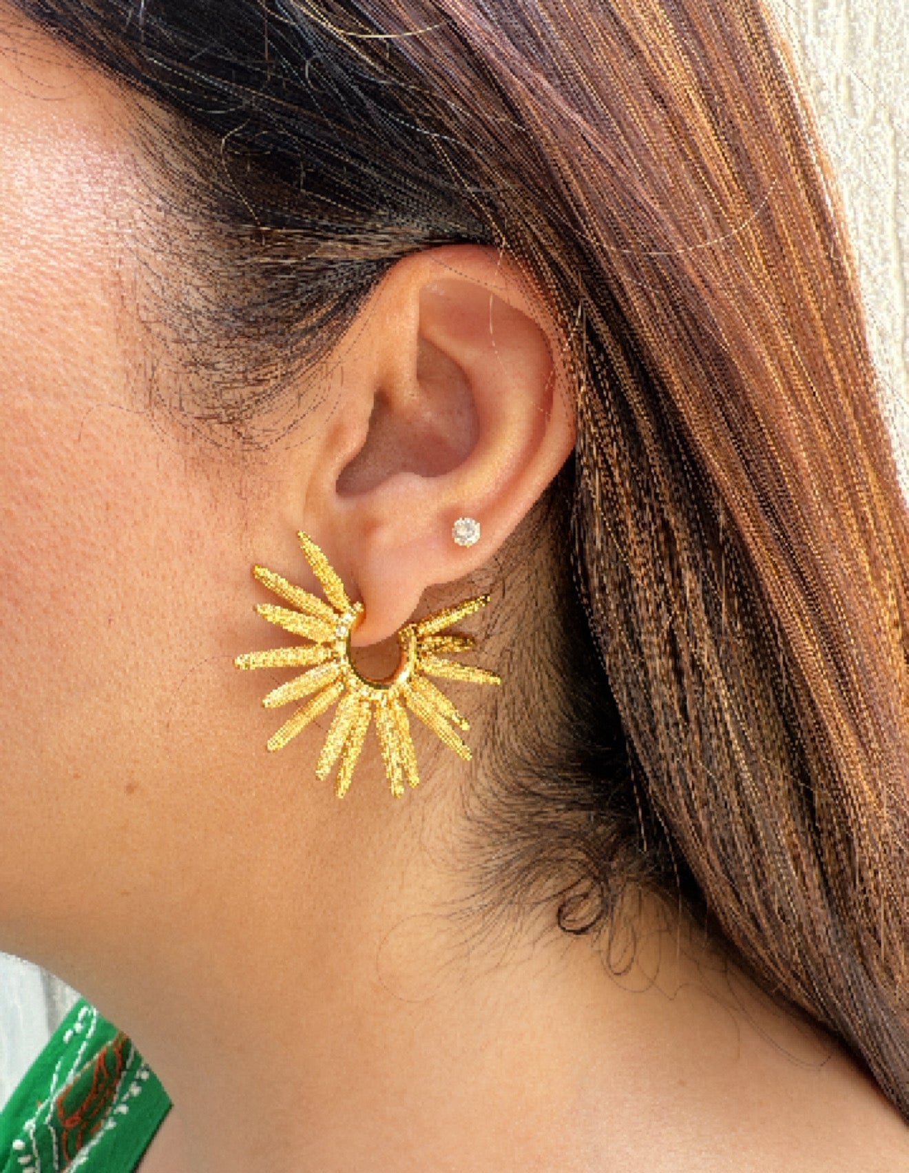 A person wearing gold-plated textured sun rays Hoop earrings.