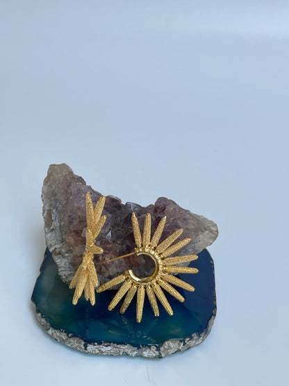 Sun hoop Earrings with gold plating on a blue stone surface background