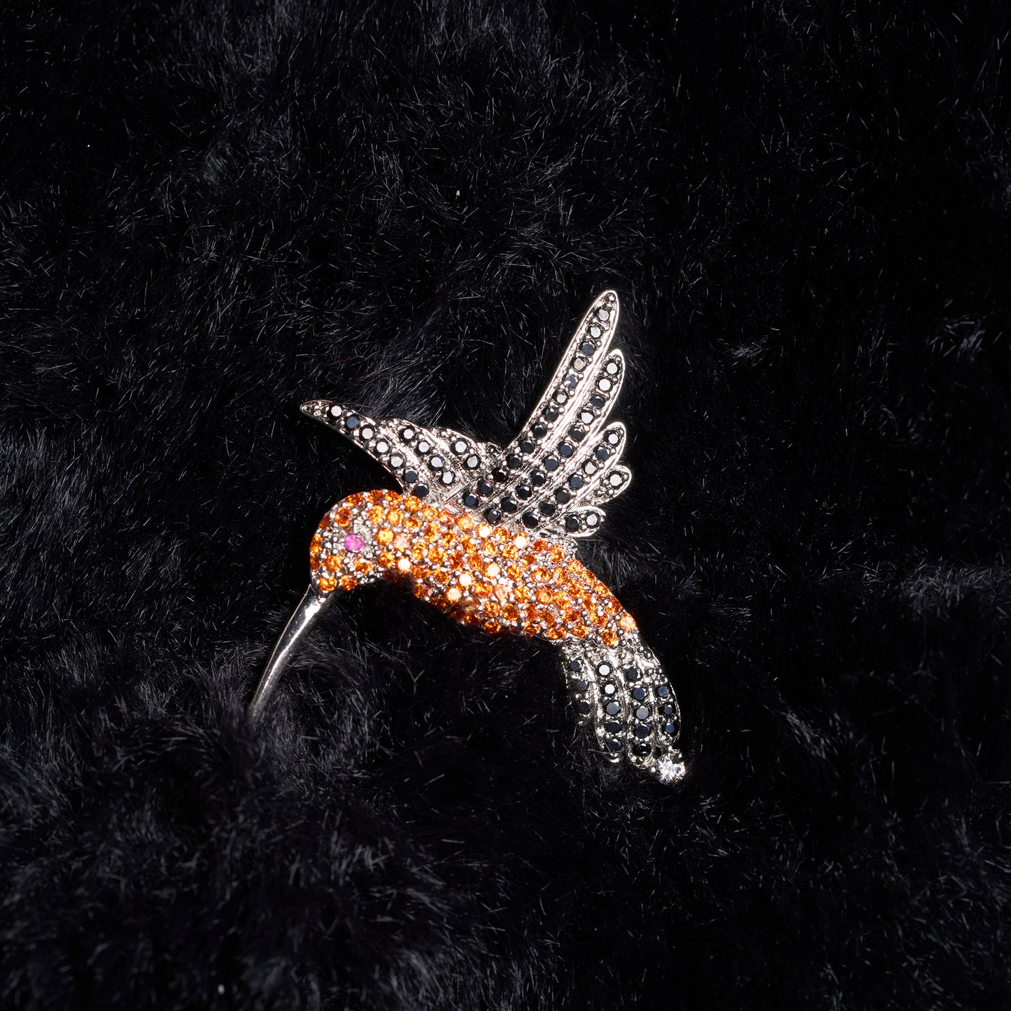 Decorative hummingbird brooch with orange and silver design on a black textured background