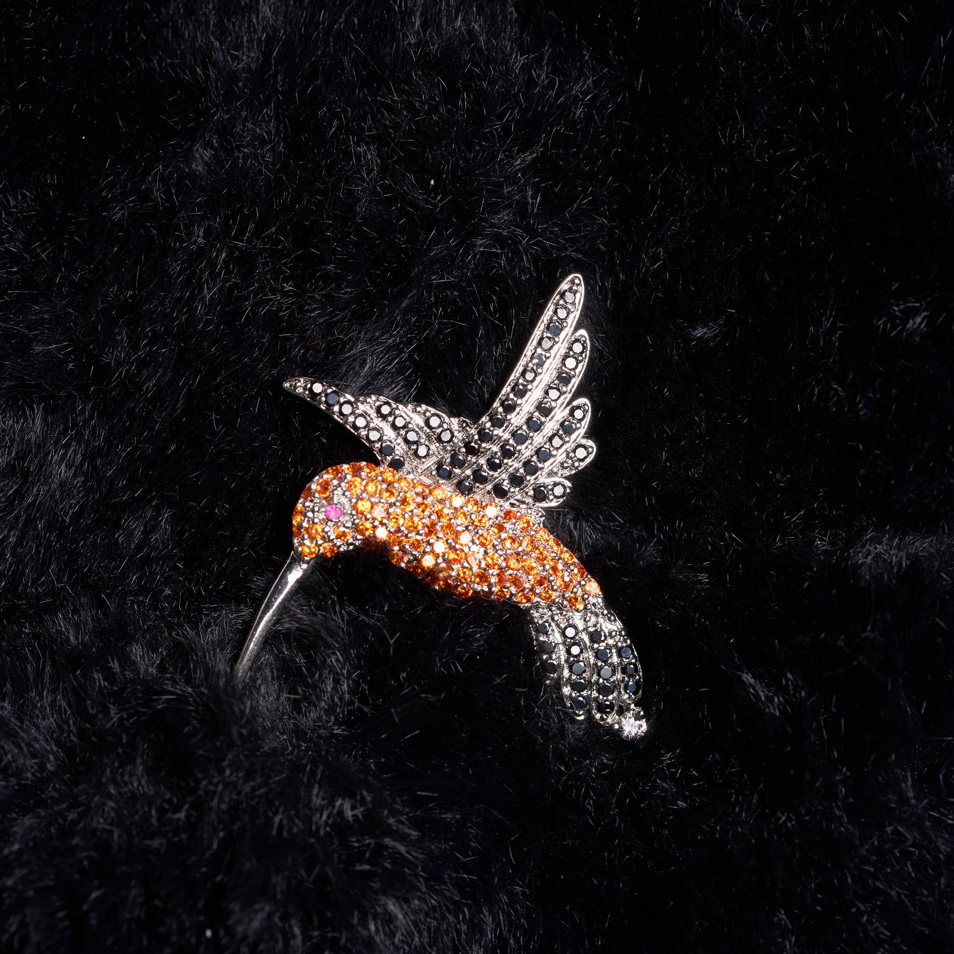 Decorative hummingbird brooch with orange and silver design on a black textured background